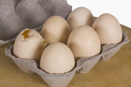 Broken egg in a carton with other eggs