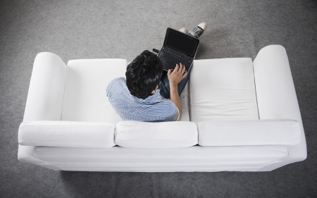 High angle view of a man sitting on a couch working on a laptopの写真素材