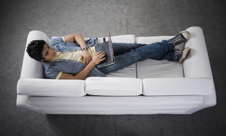 High angle view of a man lying on a couch working on a laptopの写真素材