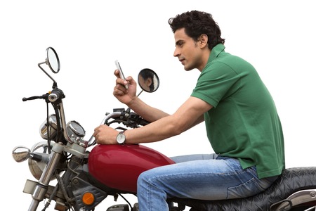 Man text messaging on a mobile phone while sitting on a motorcycleの写真素材