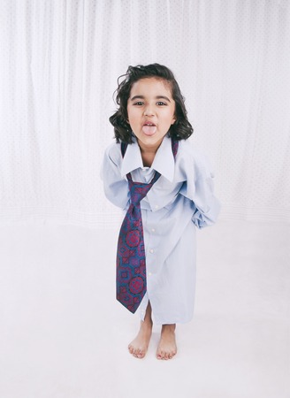Portrait of a girl wearing oversize shirt with tie and sticking her tongue outの写真素材
