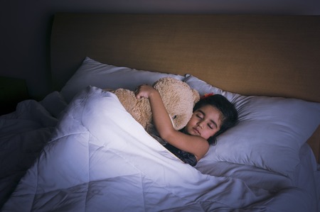 Girl sleeping on the bed with a teddy bearの写真素材