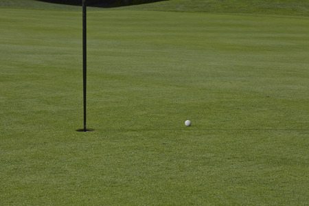 golf ball close to the cup with the flag still inの写真素材