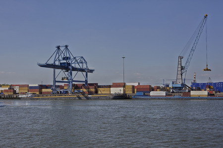 Port activity in the port of Rotterdam. Two cargo ships are delivering containers, that are unloaded...