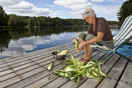 Woman shucking corn by a lake の写真素材
