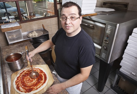 Chef making a pizza spreading sauce の写真素材