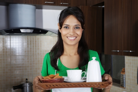 Woman holding tea cup, kettle and biscuits in a trayの写真素材