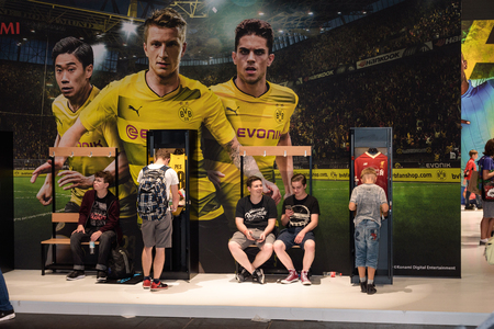 Cologne, Germany - August 24, 2017: Boys stand and sit in front of a BVB advertisement for Pro Evolution Soccer from the company Konami at Gamescome 2017. Gamescom is a trade fair for video games held annually in Cologne.のeditorial素材