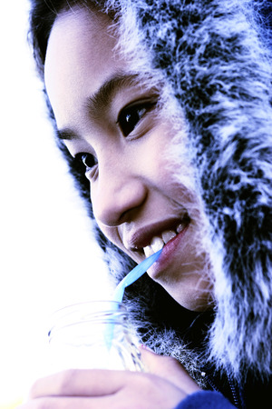 Close-up picture of a young girl in furry jacket drinking water