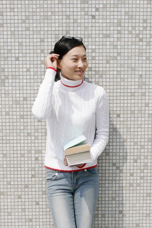 Girl leaning against the wall holding a stack of books.