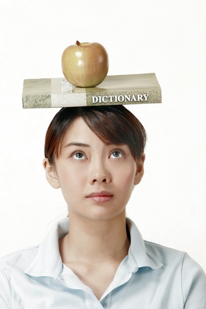 Woman looking up while balancing a dictionary and an apple on her head