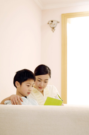 Woman and boy reading book at homeの写真素材