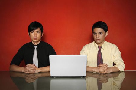 Two businessmen sitting at a table with laptop in the middleの写真素材
