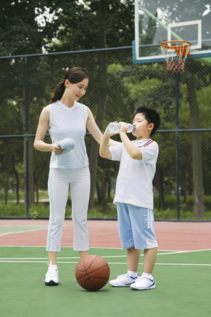 Boy drinking water, woman watchingの写真素材