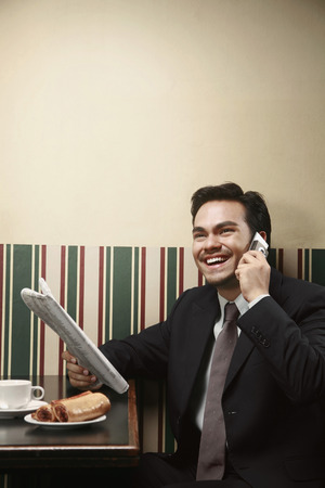 Businessman talking on the phone while holding newspaperの写真素材
