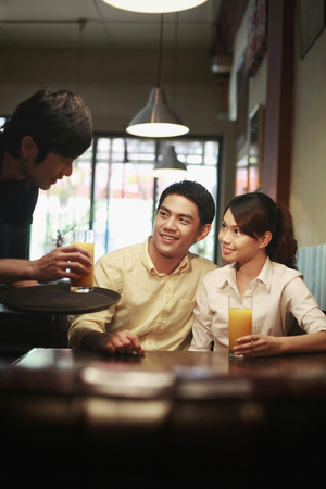 Man and woman being served drinks by a waiterの写真素材