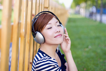 Woman listening to music while leaning against the fenceの写真素材
