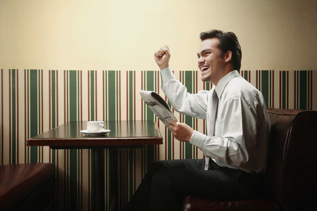 Businessman cheering while reading newspaperの写真素材