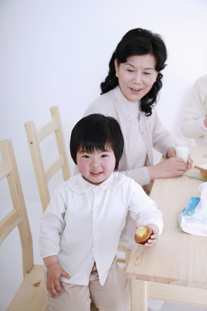 Girl smiling while holding muffin, senior woman looking at herの写真素材