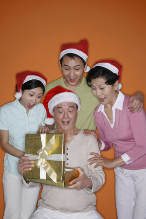 Senior man opening present, the rest watching in surpriseの写真素材