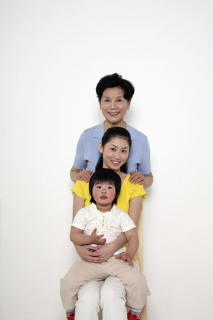 Girl sitting on woman's lap, senior woman standing behind themの写真素材