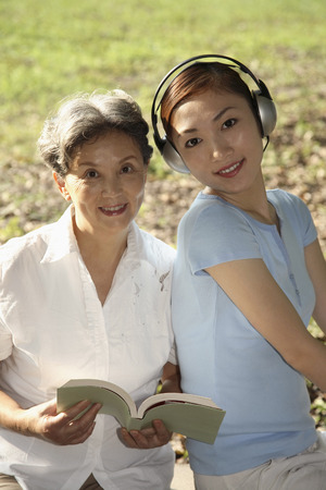 Woman listening to headphones while senior woman is holding a bookの写真素材