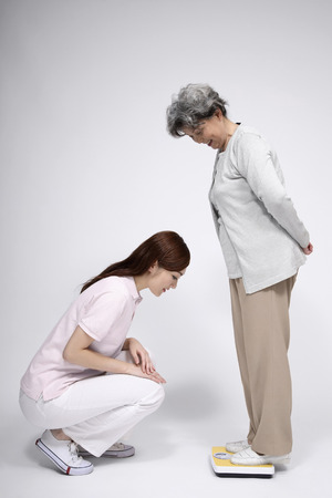 Senior woman on scale while woman is checking her weightの写真素材