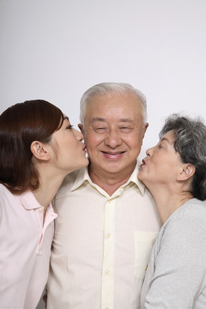 Senior man getting kisses from senior woman and womanの写真素材