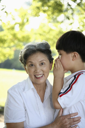 Boy whispering to senior womanの写真素材