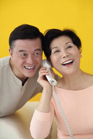 Senior woman talking on the phone, senior man trying to listenの写真素材