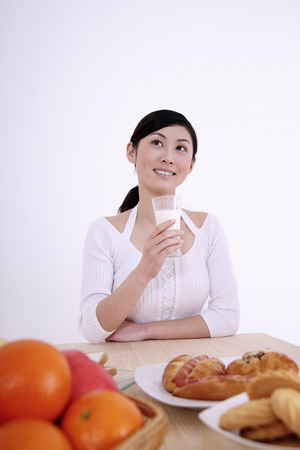 Woman looking up while holding a glass of milkの写真素材