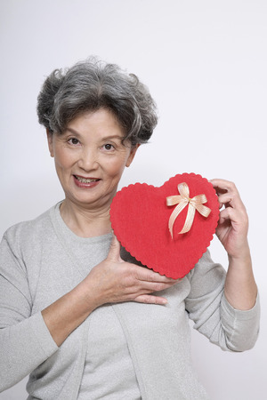 Senior woman holding heart-shaped gift boxの写真素材