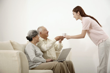 Senior man and woman using laptop while woman serves senior man with teaの写真素材