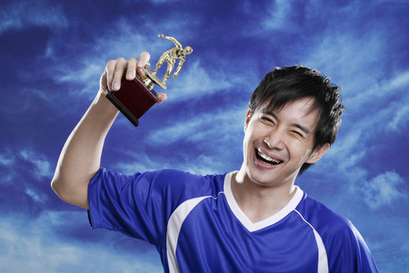 Man holding trophy in air, smilingの写真素材