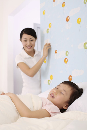 Woman switching off lights while girl is sleepingの写真素材