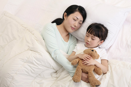 Woman and girl sleeping, girl hugging soft toyの写真素材
