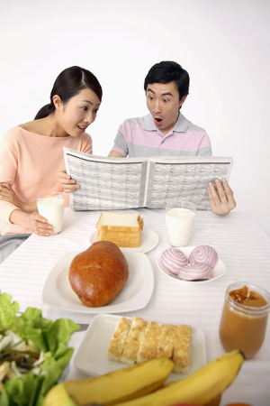 Man and woman reading newspaper over breakfastの写真素材