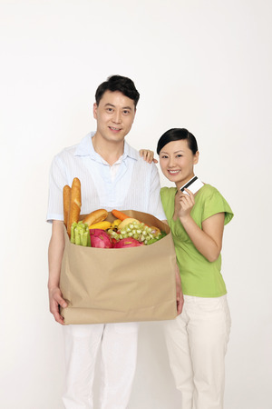 Man holding a bag of groceries, woman holding credit card smilingの写真素材