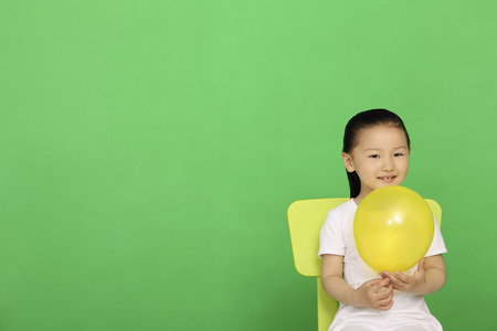 Girl sitting on chair holding a balloonの写真素材