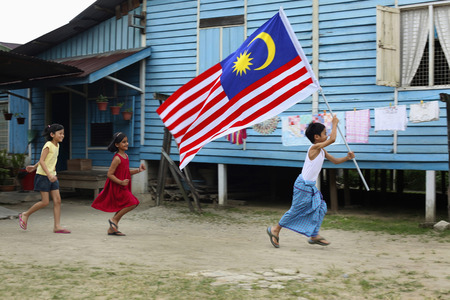Boy running with flag in hands, girls running behind himの写真素材