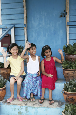 Children waving while sitting on stairsの写真素材