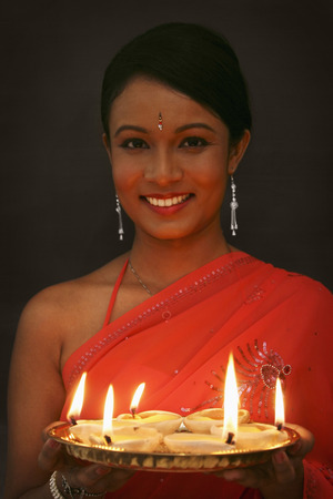 Woman holding a tray of lit oil lamps, smilingの写真素材