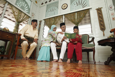 Boy reading greeting card with parents, senior man watchingの写真素材