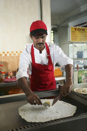 Man preparing roti tisu, putting margarine on flattened doughの写真素材