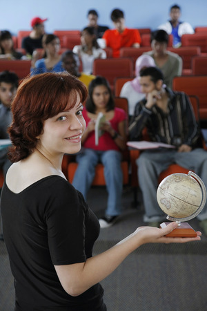 Woman holding a globe looking at the camera with students in the backgroundの写真素材