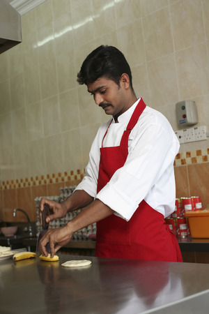 Man cutting banana into pieces, preparing to make roti pisangの写真素材
