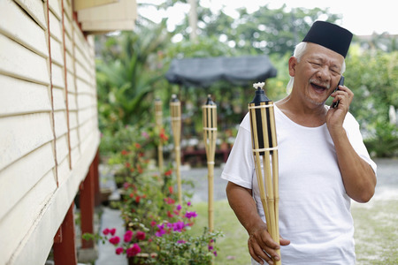 Senior man holding bamboo torch while talking on the phoneの写真素材
