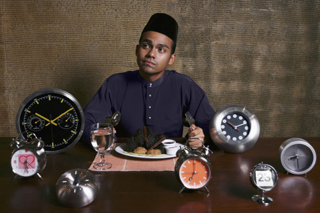 Man enjoying his meal with different type of alarm clocks on the tableの写真素材