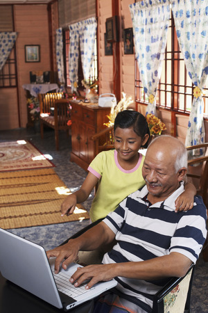 Senior man and granddaughter using laptopの写真素材