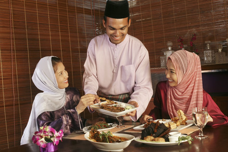 Man passing a plate of satay to his friends Man passing a plate of satay to his friends